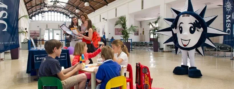 Des enfants à une table et la mascotte MSC en fond