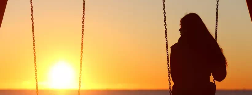 Femme de dos, seule et regardant vers le coucher ou le lever de soleil au loin