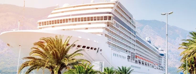 grand bateau de croisière au large de la mer avec des palmiers au premier plan et des montagnes à l’