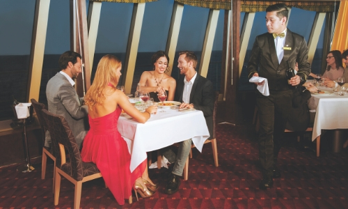 Groupe de personnes mangeant en s'amusant dans un restaurant du navire avec plat, verre de vin et serveur à côté